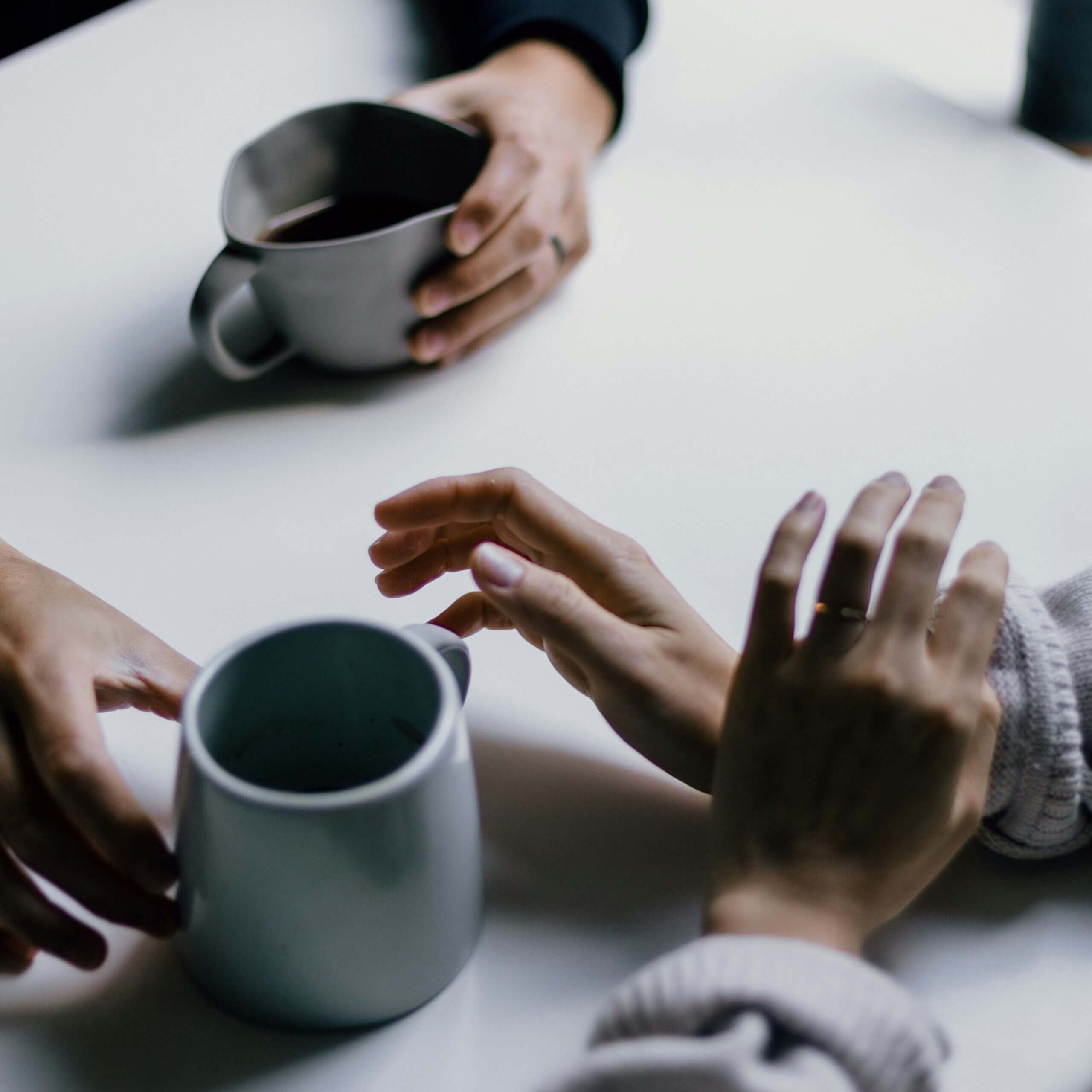 Zwei Personen sitzen sich gegenüber halten Becher, eine gestikuliert, Symbol für Kommunikation und Strategie