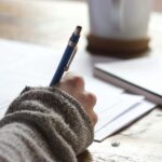 Hand schreibt mit Stift auf Papier, Symbol für technische und inhaltliche Optimierung